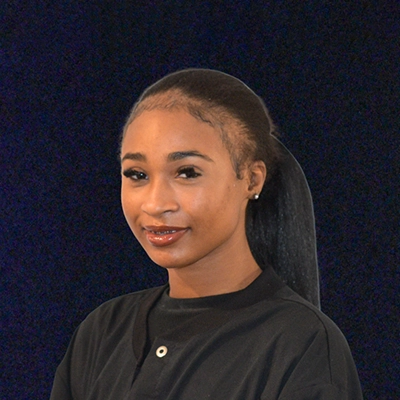 Scheduling & Treatment Assistant Mikia Smiling In Front Of Dark Blue Background